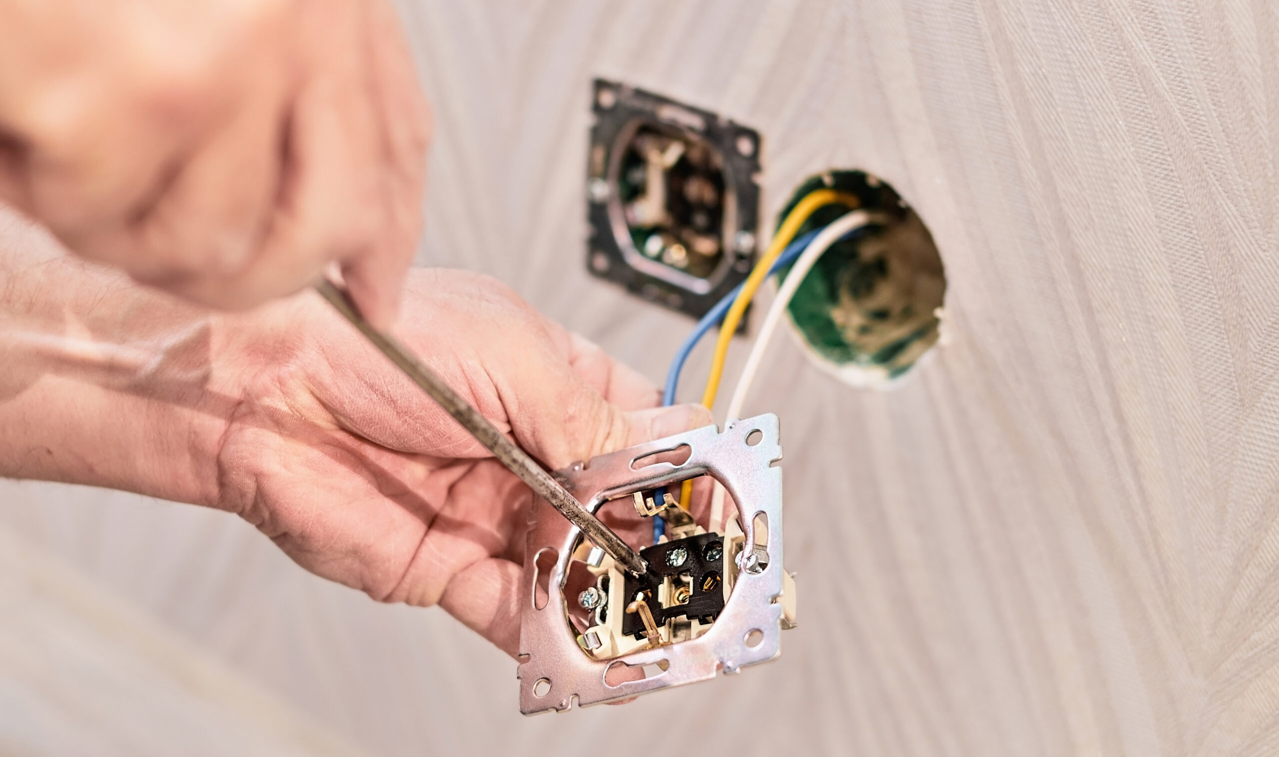 Hands of an electrician installing an electrical outlet in a new house. Assembly of the electrical network in the room, installation of the electrical network
